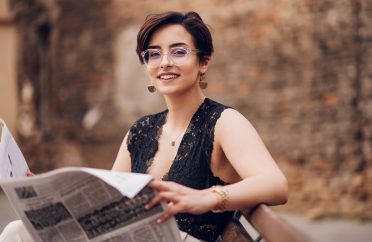 Stylish retro woman reading newspaper while sitting on the bench outside